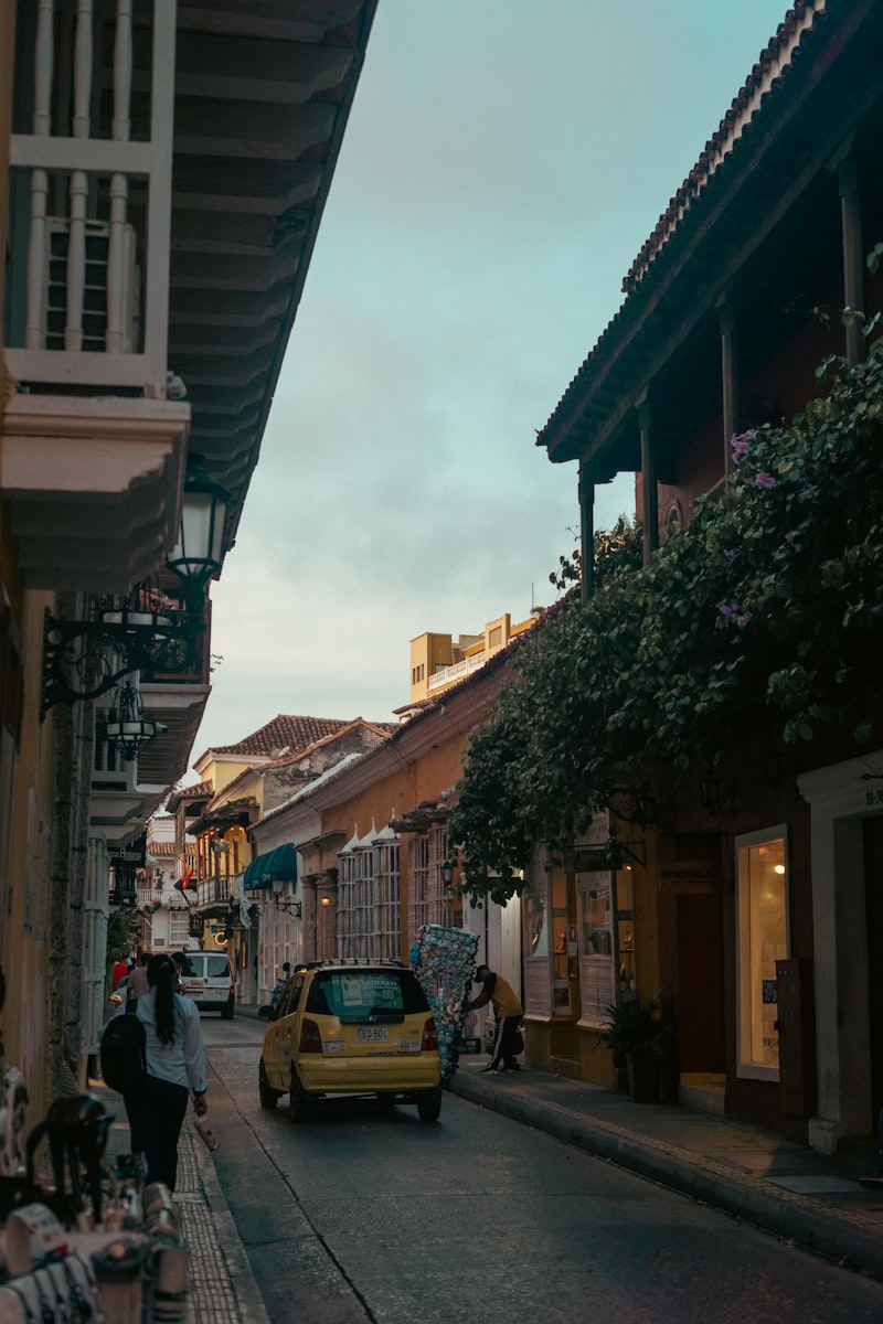 Historic street with balconies, a yellow car, and a pedestrian.